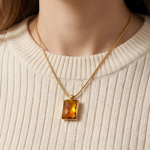 Close-up of amber square glass pendant on 18K gold-plated snake chain with knit sweater