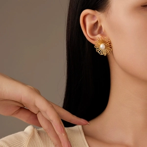 Elegant gold flower stud earrings with white pearl center worn on a model's ear