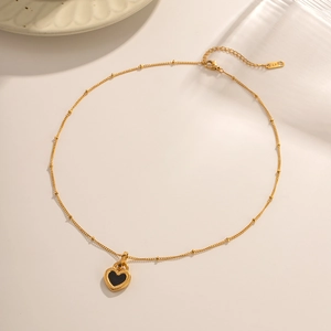 Detailed top view of a gold-beaded chain with a black heart pendant on a soft background