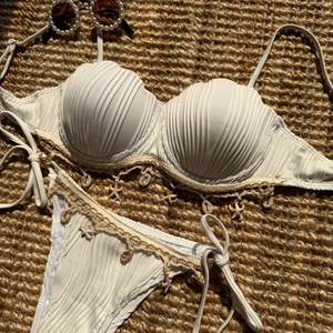 Detail of cream white textured bikini with seashell charms on a woven beach mat