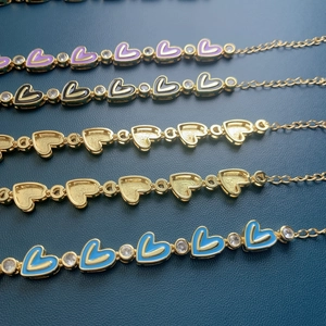 Detail of gold heart link bracelet with colorful enamel and zircon on dark leather