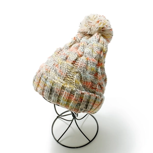 Close-up of thick cable knit pattern on a multi-colored beanie with large faux fur pompom