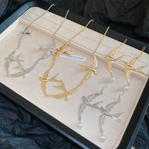 Detailsatz Schwalben-Anhänger und Perlenohrringe in Gold und Silber auf einem Display
