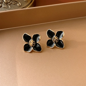 Macro shot of vintage black four-leaf flower stud earrings with gold edges on a tray