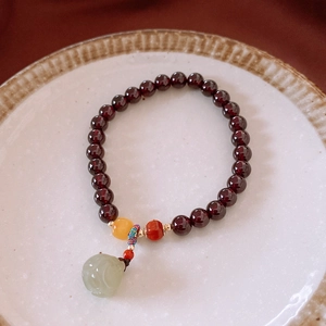 Makroaufnahme von Granatperlen-Armband mit Hetian-Jade-Lotusanhänger auf Keramik