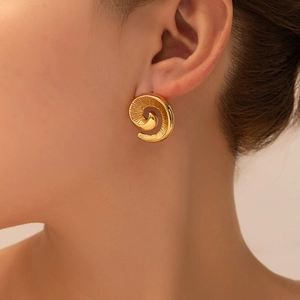 Close-up of golden spiral stud earring with radial textures on model's ear