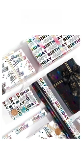 Close-up of holographic gold Happy Birthday wrapping paper rolls and gift boxes