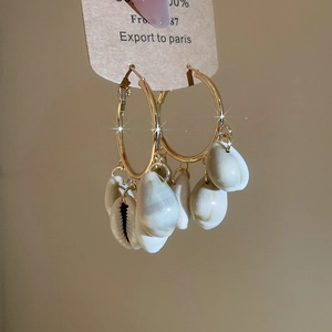 Detail of bohemian gold hoop earrings featuring natural white cowrie shell pendants