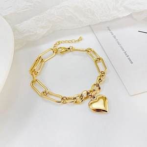 Detailed view of a gold heart pendant and oval chain bracelet on a white textured background