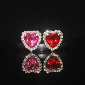Heart crystal stud earrings in pink and red with diamond accents on black mirror surface