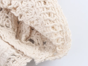 Macro shot of intricate beige crochet knit fabric showing delicate hollow lace patterns