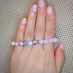 Dettaglio di perle in pietra naturale rosa e floreale con perla dorata su una mano