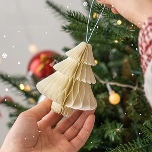 Mini cream white honeycomb paper Christmas tree ornament held in hands with warm background