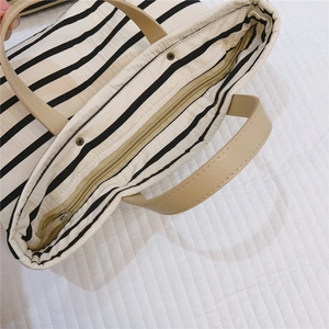 Top view of striped canvas tote bag showing metal zipper closure and brown handles