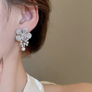Close-up of flower earrings with zircons and hanging pearls worn on ear