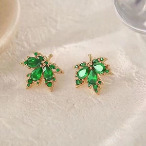 Gros plan de boucles d'oreilles feuille d'érable dorées avec pierres vertes et zircons