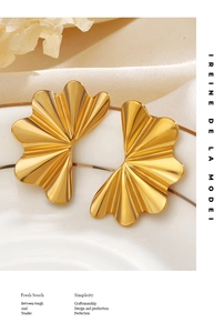 Détail des boucles d'oreilles dorées en forme de coquille sur une assiette en céramique