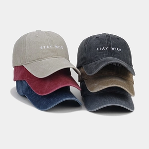 Dettaglio del ricamo Stay Wild su vari colori di cappellini da baseball in cotone lavato