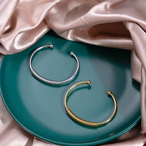 Detail of gold and silver knot bangles with spiral texture on green tray with satin