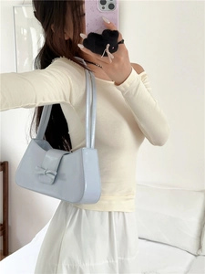 Detail showing light blue underarm bag with a bow decoration in a bright minimal room