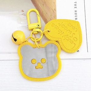 Cute yellow bear keychain with mirror face, heart charm and bell on white table