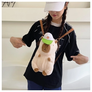 Detail of plush capybara crossbody bag featuring a white and green baseball cap