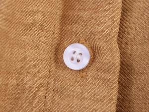 Macro view of a white button on camel twill fabric with visible linen texture