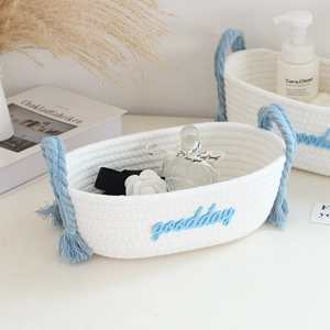 Detail of white cotton woven storage basket featuring blue fringe and goodday embroidery
