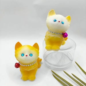 Two yellow flocked cat figurines with pearl collars and bells in a still life setting
