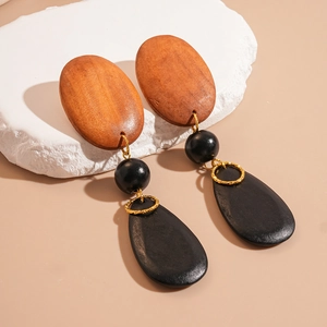Detailed close-up of geometric wood and gold metal earrings on a natural stone base