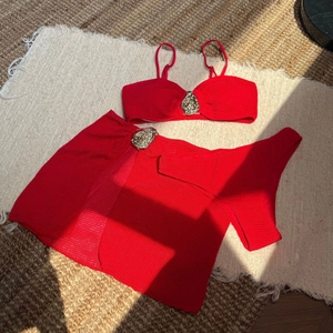 Detail of red ribbed three-piece bikini with mini skirt and golden lion emblems