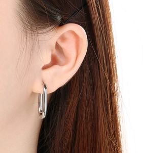 Close-up of a silver-tone oval U-shaped stainless steel earring worn by a model