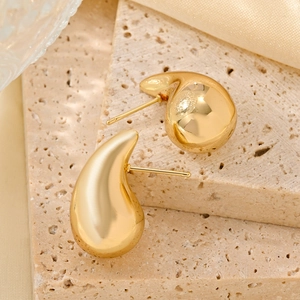 Detailed view of gold teardrop earrings placed on natural beige travertine stone