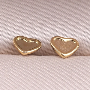 Macro shot of minimalist gold heart stud earrings on soft silk fabric background