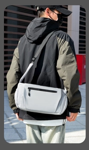 Detail shot of a grey waterproof messenger bag on a model showing side strap and zipper pocket