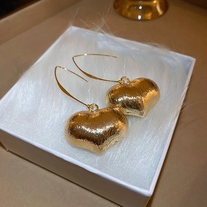 Detail of large heart-shaped drop earrings with brushed gold metal texture in a gift box
