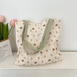 Detail of pleated tote bag with cute bear pattern and contrasting green straps on a desk
