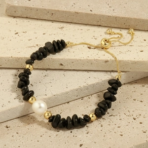 Detail of handmade bracelet with black gravel, white pearl and adjustable gold chain