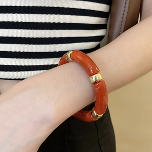 Detail view of chunky iridescent acrylic bracelet with orange segments and golden beads
