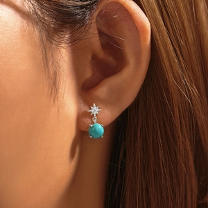 Close-up of a model wearing a turquoise bead earring with a silver star-shaped diamond stud