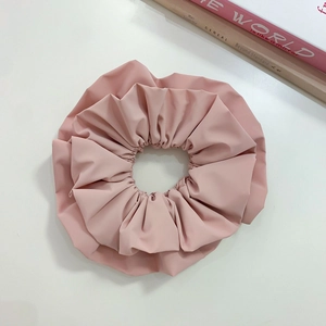 Detailed close-up of light pink faux leather scrunchie with layered pleats on white surface
