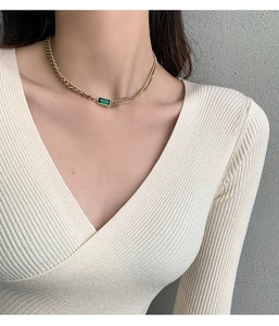 Detail of 18K gold titanium chain necklace featuring emerald green gemstone on a model