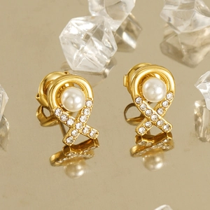 Boucles d'oreilles ruban plaqué or 18K avec perle et cristaux sur surface réfléchissante