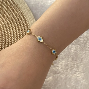 Gold Hamsa Hand bracelet with blue evil eye charms worn on a wrist over soft fabric