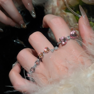 Close-up of pink heart bow rings with pavé diamonds on a model's hand with soft feathers