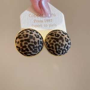 Macro detail of round leopard print earrings with gold plating on display card