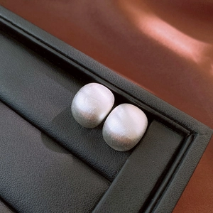 Vue macro de boucles d'oreilles carrées argentées avec finition métal brossé sur cuir