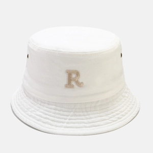 Close-up of white cotton bucket hat featuring beige R letter embroidery and metal eyelets