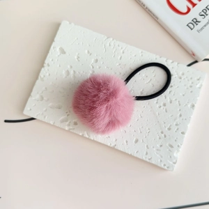 Detail view of a fluffy pink faux fur pompom hair tie with elastic band on a white texture