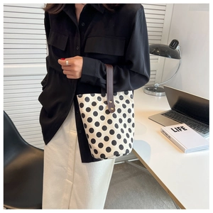 Close-up of polka dot canvas bucket bag with brown handles on a minimalist office desk